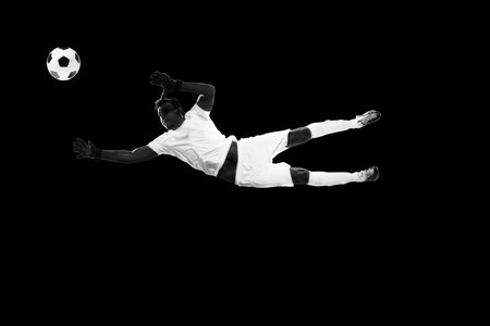 Determined sportsman, football player in motion with ball, training isolated on black background. Monochromeの写真素材