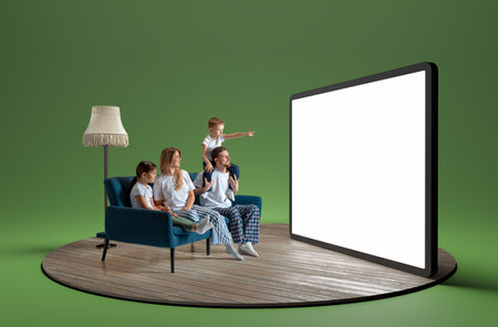 Happy young family in pajamas, man, woman and children sitting on sofa and looking at giant 3D model of tablet with empty screenの写真素材