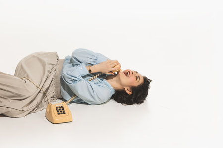 Happy, emotional, young woman lying on floor and talking on retro style phone, having fun on...