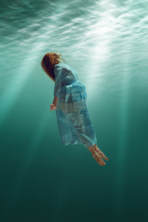 Free spirit. Tender redhead young girl in elegant dress depicted in underwater scene, showing...