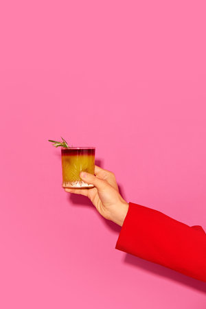 Female hand holding cocktail with orange juice against pink background. New York sour traditional cocktailの写真素材