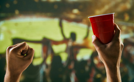 Sport fans raising hands to support favorite football team. Gathering at stadium to watch competition, drinking beer and shoutingの写真素材