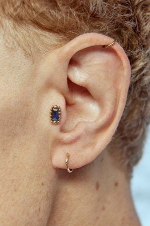 Close-up of male ear with piercing. Male model having curly hair and freckled skin
