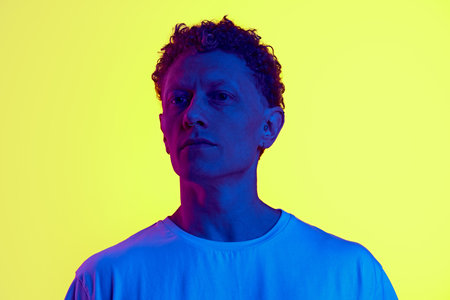 Portrait of man with curly hair standing with serious face, looking, posing against yellow...