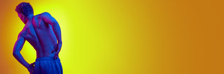 Rear view of shirtless man with relief, strong back posing against yellow background with blue neon lightの写真素材