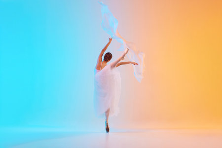 Elegant ballet dancer in white ensemble gracefully move with fabric in neon light against blue-orange gradient background.の写真素材