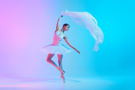 Portrait of young ballerina dancing with light transparent fabric in neon light against vivid gradient background.の写真素材