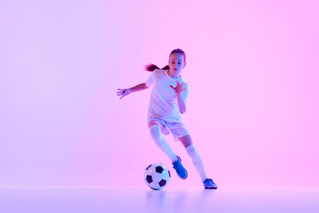 Concentrated teen girl, soccer player training, dribbling ball against pink studio background in neon lightの写真素材
