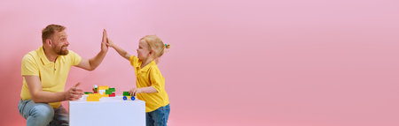Banner. Little boy give high five his father while they playing together against pink studio...
