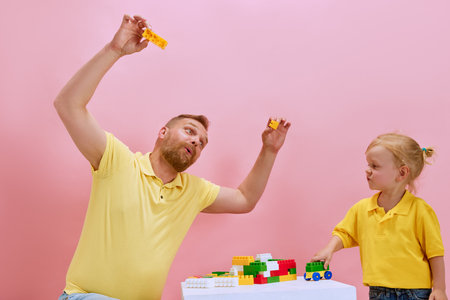 Building memories together. Father and his little son construct toy with colorful building kit against pink studio background.の写真素材