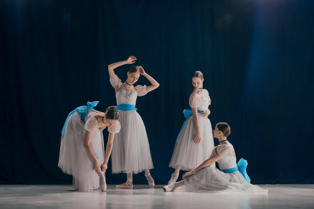 Four young tender ballerinas dressed in delicate white tutus with blue sashes gracefully pose...