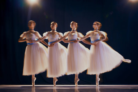 Charming young girls, ballet dancers in white tutus with blue bows on pointe dancing in motion on stage. Photo with motion blur.の写真素材
