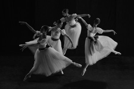 Black and white photo of young female ballet dancers in synchronized motion, their white tutus creating fluid harmony of blurred eleganceの写真素材
