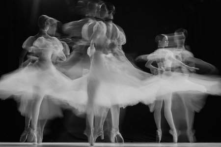 Ghostly silhouettes of ballerinas performing pirouettes on stage. Black and white photo with long exposure. Timeless.の写真素材