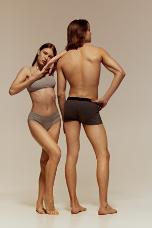 Tenderness and passion. Full-length image of muscular shirtless man and elegant young woman with slim body, models posing in cotton underwearの写真素材