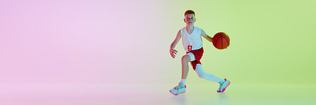 Concentrated 11 years old boy in uniform during basketball game, player in motion with ball against gradient background in neon lightの写真素材