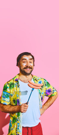 Smiling, young man in funky tropical shirt posing with barbecue sausages on fork against pink studio background.の写真素材