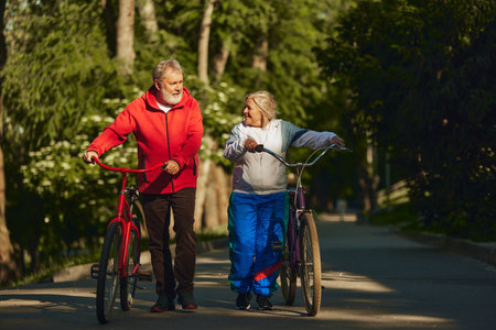 Senior couple, smiling, happy man and woman, joyfully bicycles through park, showing enduring spirit and love for outdoor activitiesの写真素材