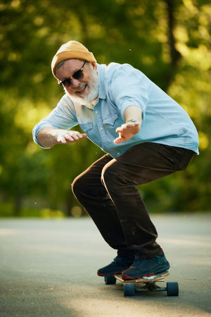 Old School Skater. Senior man in casual stylish clothes enjoying active morning in park, skateboarding on empty path.の写真素材