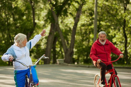 Cycling Activity. Elderly couple, man and woman, riding bicycles in lush park on warm summer day. Emotional happy peopleの写真素材