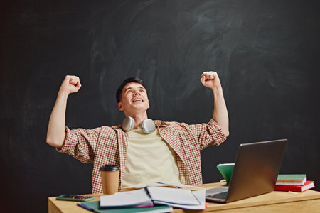Young man, student raising hands in success and joy, getting highest mark on exams. Moment of success.の写真素材