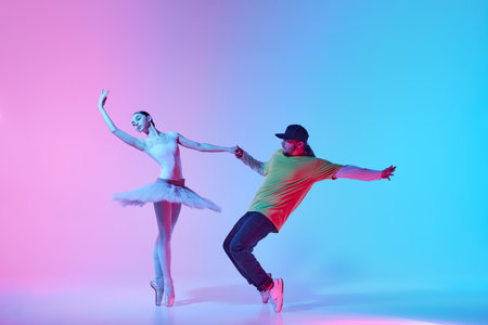 Tender young girl, beautiful ballerina dancing in tutu on pointe with energetic man, break dancer n gradient background in neon lightの写真素材