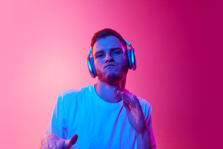 Dj. Portrait of young man in white t-shirt listening to music in headphones, and dancing against...
