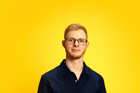 Bearded redhead young man in glasses, wearing black shirt, posing with little smile, looking at...