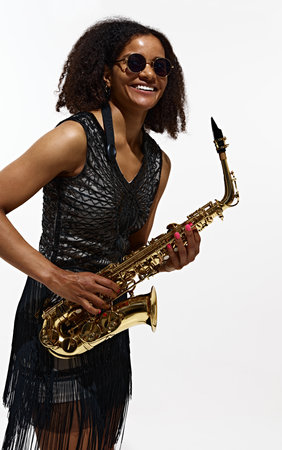 Jazz Elegance. Portrait of beautiful young woman in black dress and sunglasses, posing with golden saxophone isolated on white backgroundの写真素材