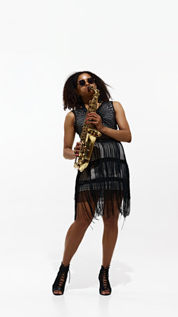 Cool Jazz Performer. Elegant female musician in eye-catching outfit playing saxophone isolated on white backgroundの写真素材