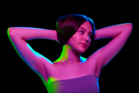 Wellness and attraction., Elegant young girl with well-kept skin and hair posing against black studio background in neon lightの写真素材