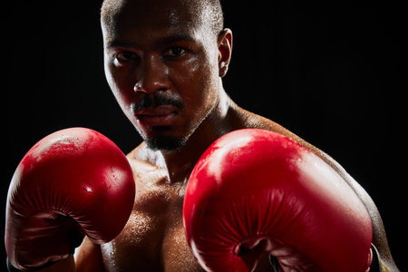 Close-up portrait of a determined boxer in red gloves, showcasing his intense focus isolated on black backgroundの写真素材