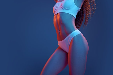 Cropped image of female body, fit buttocks against blue studio background in neon light. Anti-cellulite careの写真素材