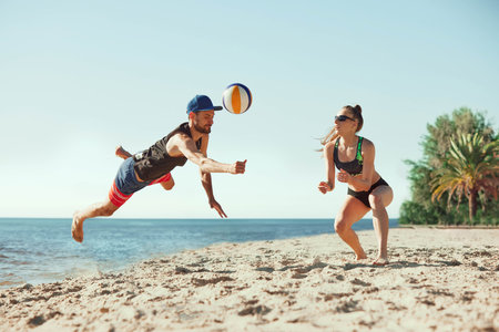 Concentrated and active young people, men and women in motion, playing beach volleyball under clear sky, in the morning by the seaの写真素材