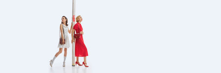 Two women dressed in elegant retro-theme dresses carrying giant cardboard tube isolated on white background. Interior designers.の写真素材