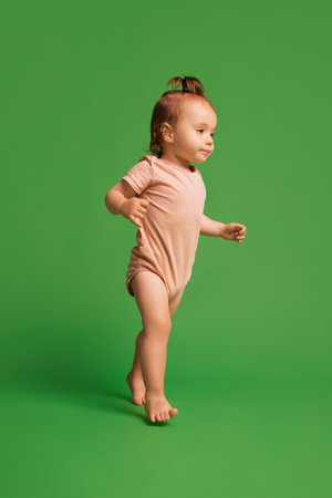 Curious little baby girl in pink bodysuit walking with isolated on green background. Learning surroundingsの写真素材