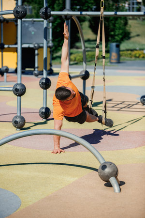 Outdoor TRX Core Workout. Muscular man in sportswear training outdoors, doing challenging trx side plank, using park equipment and strapsの写真素材