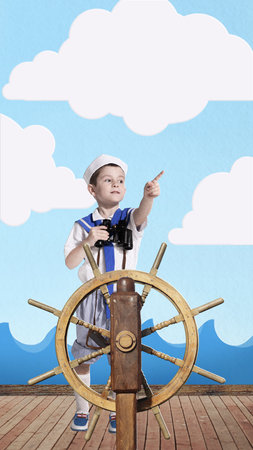 Young boy dressed as sailor standing confidently at ship helm, holding binoculars and pointing...