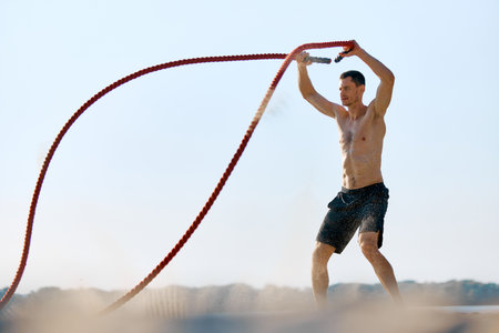 Dynamic and intensive outdoor functional training. Shirtless muscular man training with battle ropes, showing his strong body.の写真素材