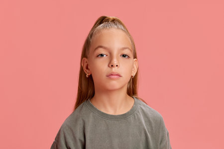 Portrait of beautiful young girl, child in casual gray t-shirt, with ponytail hairstyle standing with calm expression against peach backgroundの写真素材