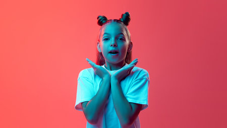 Portrait of young girl in white t-shirt, with hair styled in two buns posing against vibrant pink...