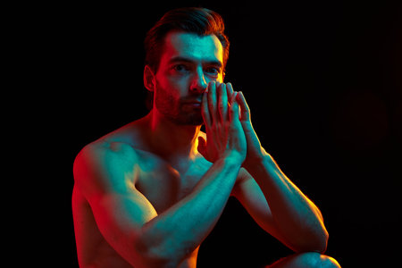 Portrait of handsome confident shirtless man with perfect sportive body and well-kept hair against black studio background in neon lightの写真素材