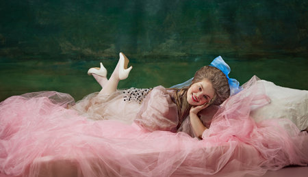 Graceful Rest. Elegant young woman, royal person lying on bed with pink veiled and smiling against vintage green background. Historical charmの写真素材