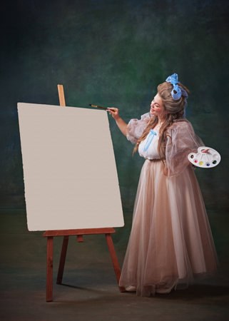 Inspired artist. Happy young woman in period attire standing with palette next to canvas and creating masterpiece, drawing against vintage green backgroundの写真素材