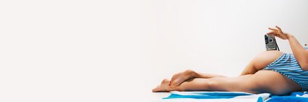 Back view, cropped image of woman wearing striped swimsuit, lying on beach towel with vintage camera...