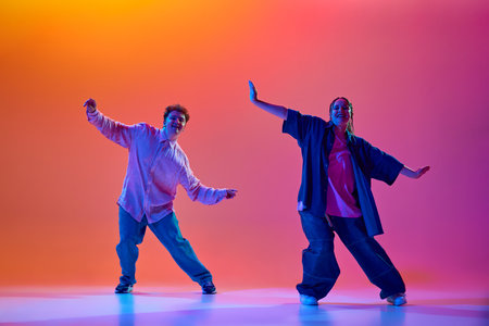 Dynamic image of young man and woman in casual oversized clothes dancing hip-hop against gradient...