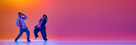 Dynamic image of talented young man and woman, dancers performing hip-hop against gradient studio background in neon lightの写真素材