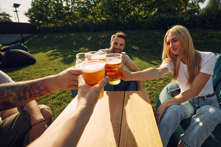 Happy young smiling people sitting outdoors in cafe, restaurant, enjoying refreshing beer, clinking glasses.の写真素材