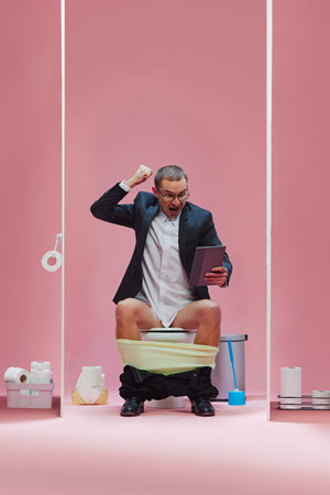 Goal. Emotional man in formal wear sitting with pants down on toilet and watching soccer game via...