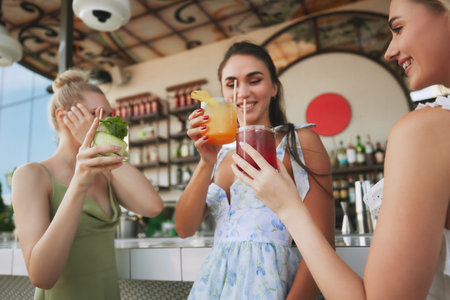 Smiling happy young women meeting on modern outdoor bar, drinking cocktails, enjoying cheerful conversation with friends. Summer vibesの写真素材
